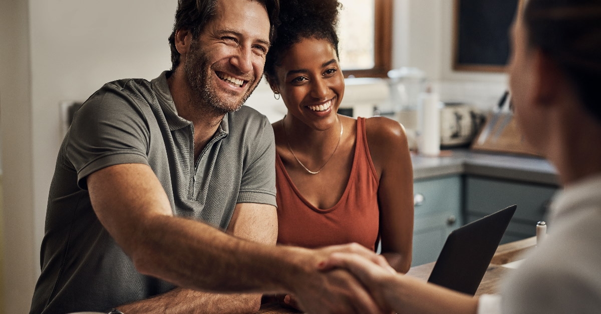 couple sitting at table shaking hand with female finance advisor