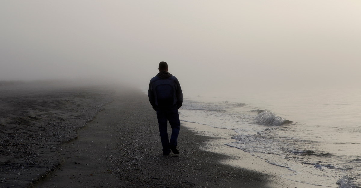 lonely man walking on sandy beach shore 