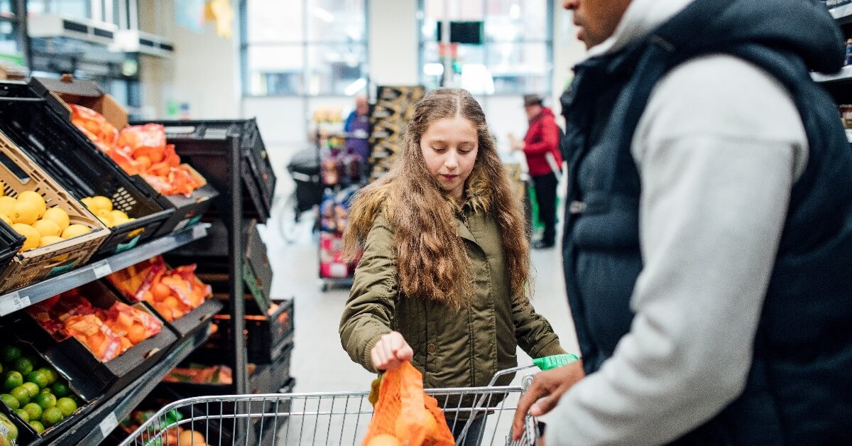 girl putting grocery into trolley while shopping with father at store