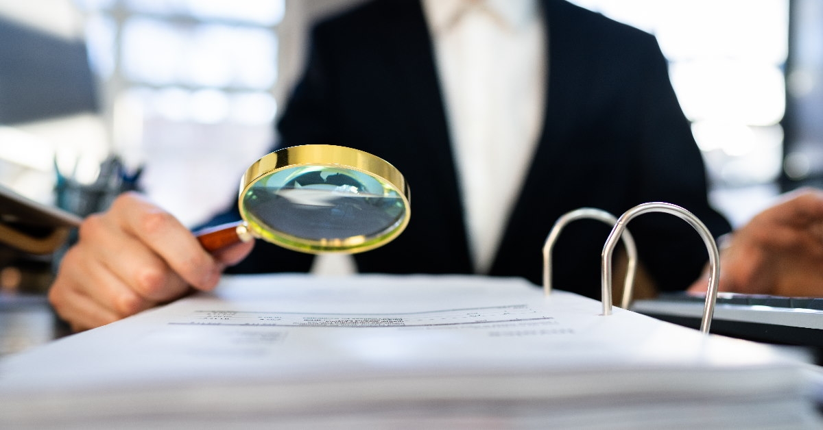 male auditor in suit using magnifying glass to check irs tax audit file on table