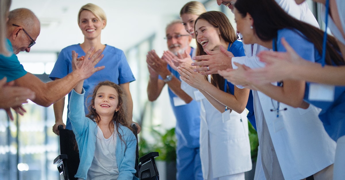 medical staff clapping for little girl sitting on wheelchair recovering from illness