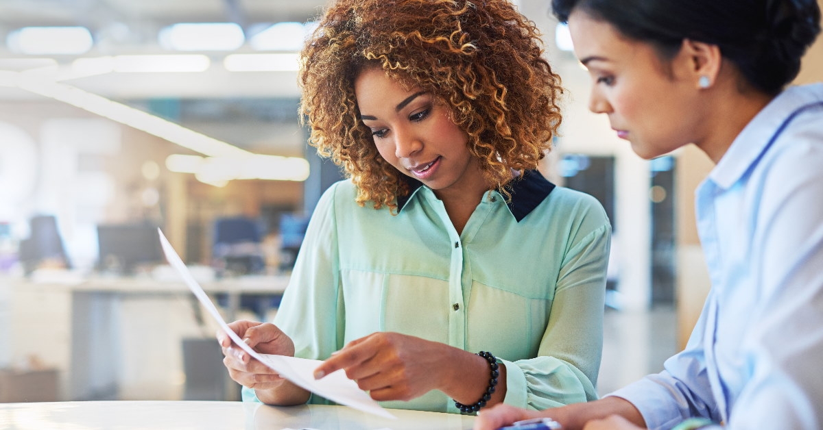 multiethnic female employees sitting at table reviewing papers in office
