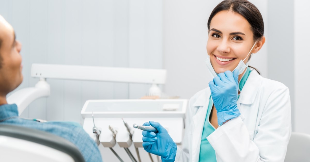 female dentist holding drill at clinic smiling besides patient