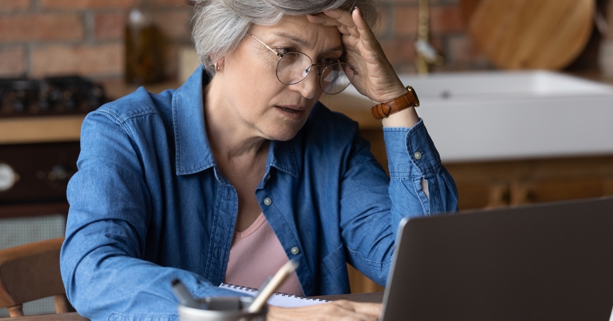 distressed mature grey-haired woman looks at laptop