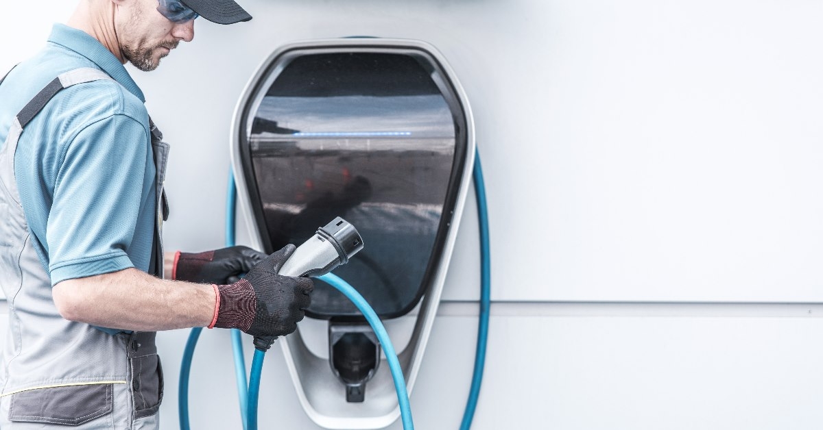 male worker standing outdoor charging cord of electric vehicle charger