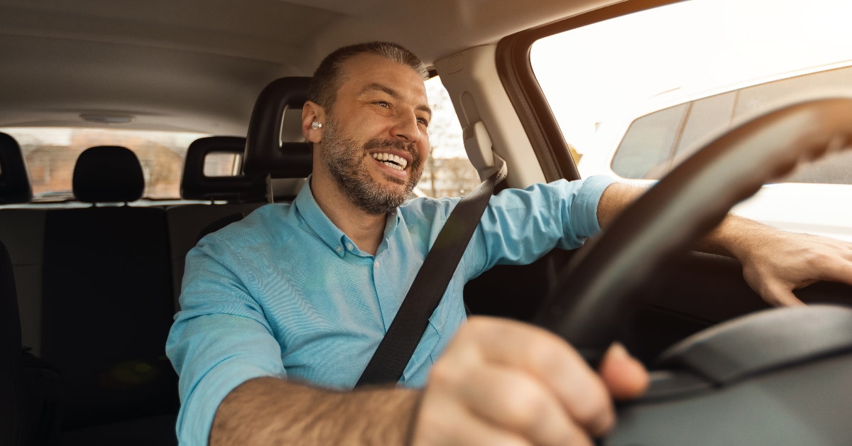 man sitting at driving seat in car wearing earpods and smiling