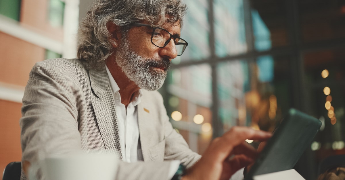mature businessman wearing suit and glasses working on tablet at cafe