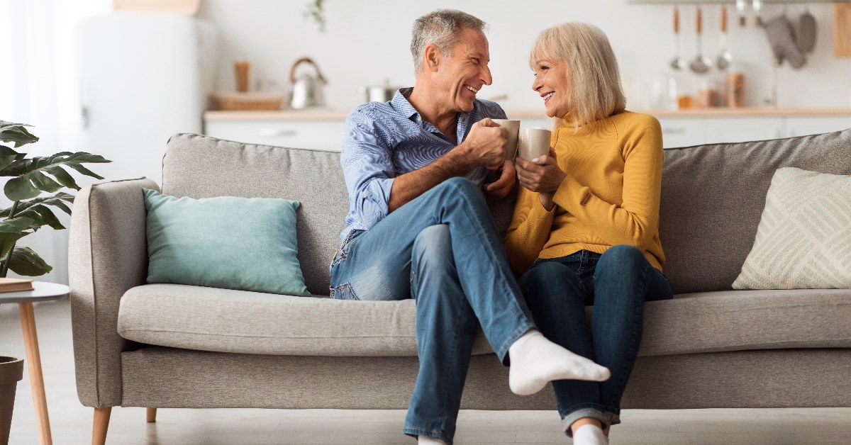 Happy senior couple sitting on couch together holding cup of coffee at home