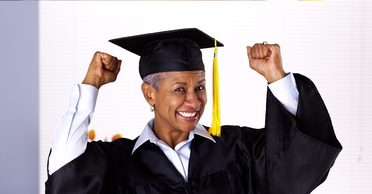 senior woman wearing graduation dress cheering while holding hands in air