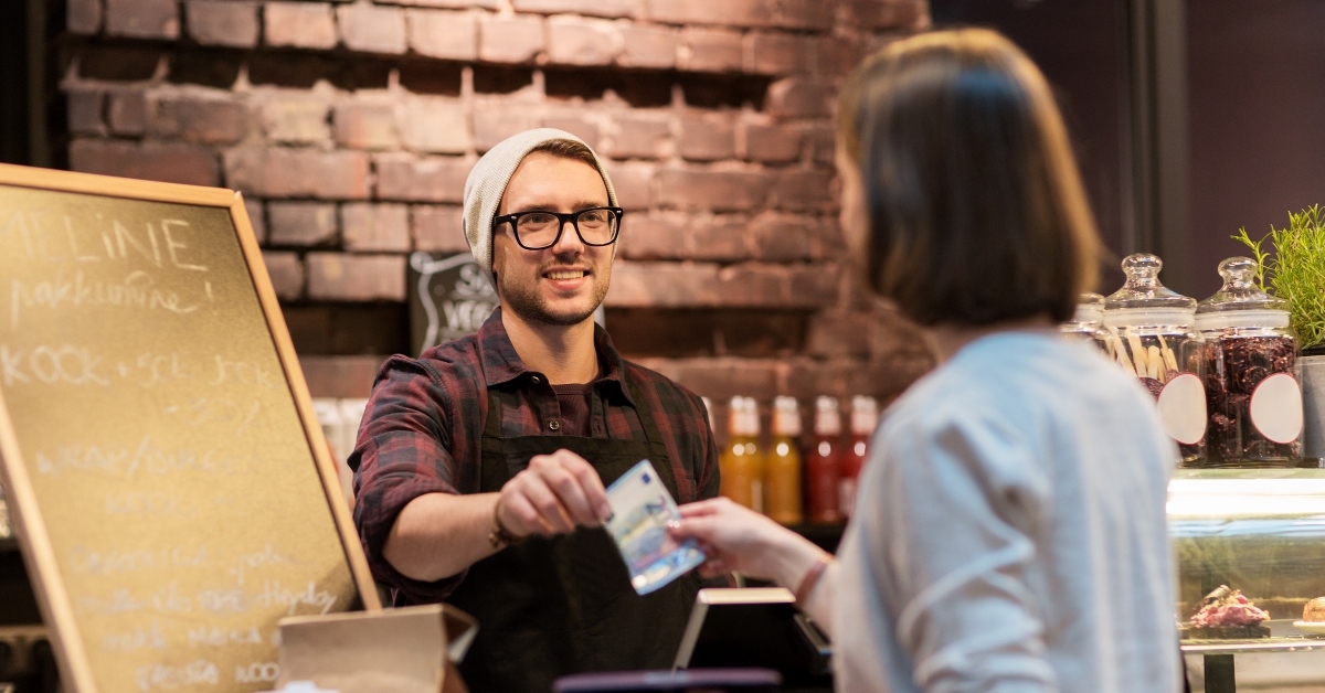 happy barman and woman paying money at cafe