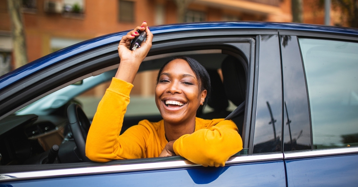 happy black woman sitting in her new car and showing keys