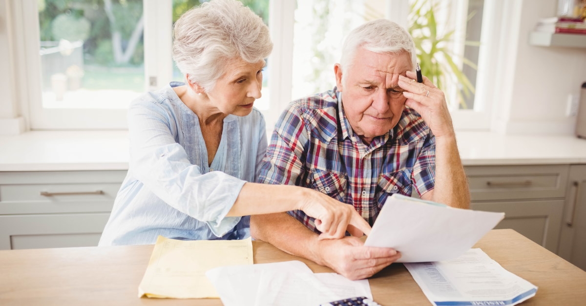 senior couple sitting at table reviewing taxes while doing calculations 