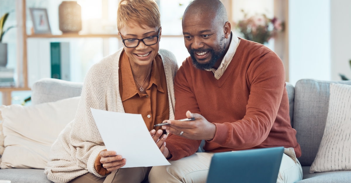 african american couple sitting on couch reviewing financial statements at home with laptop on table
