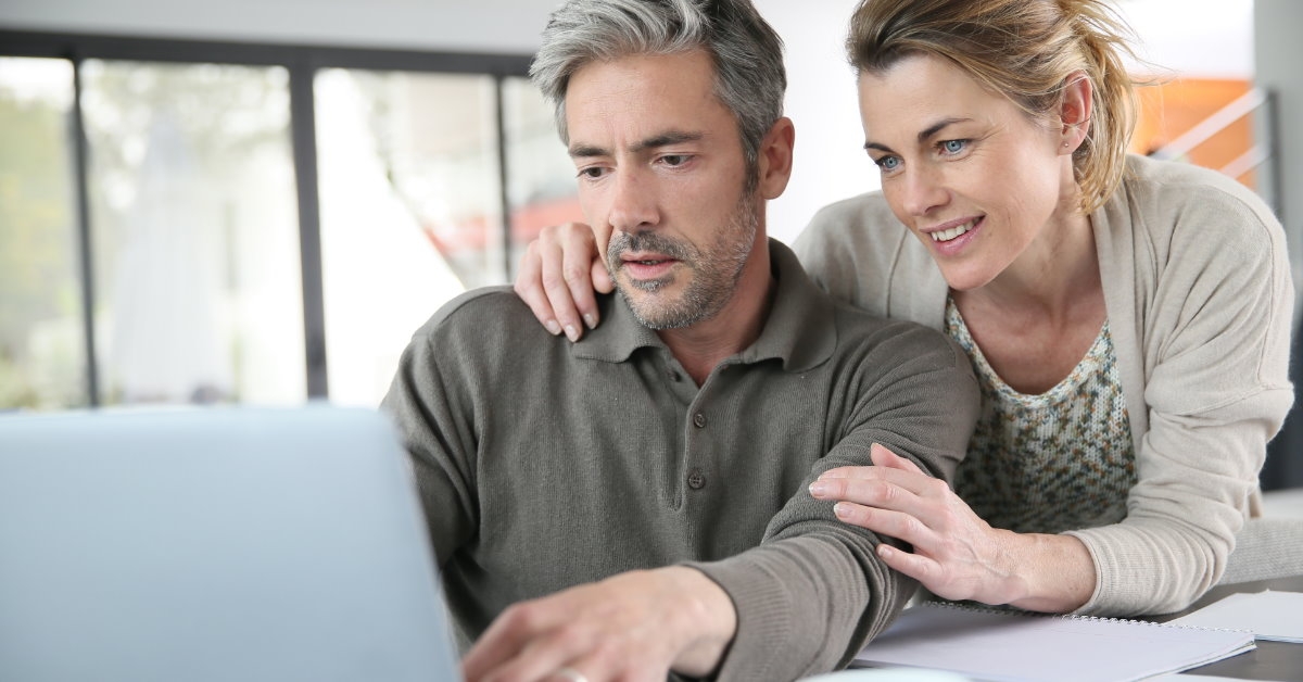 attractive senior couple reviewing financial budget using laptop with papers and cup on table
