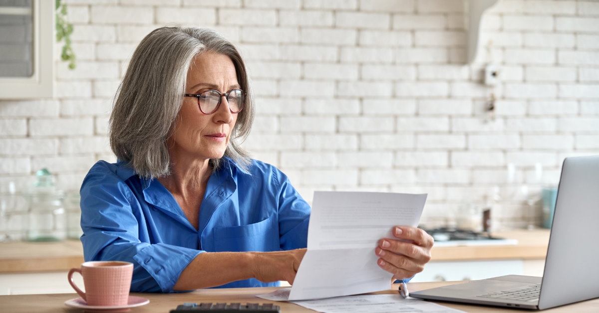 senior lady sitting at table with laptop calculator and cup reviewing taxes at home