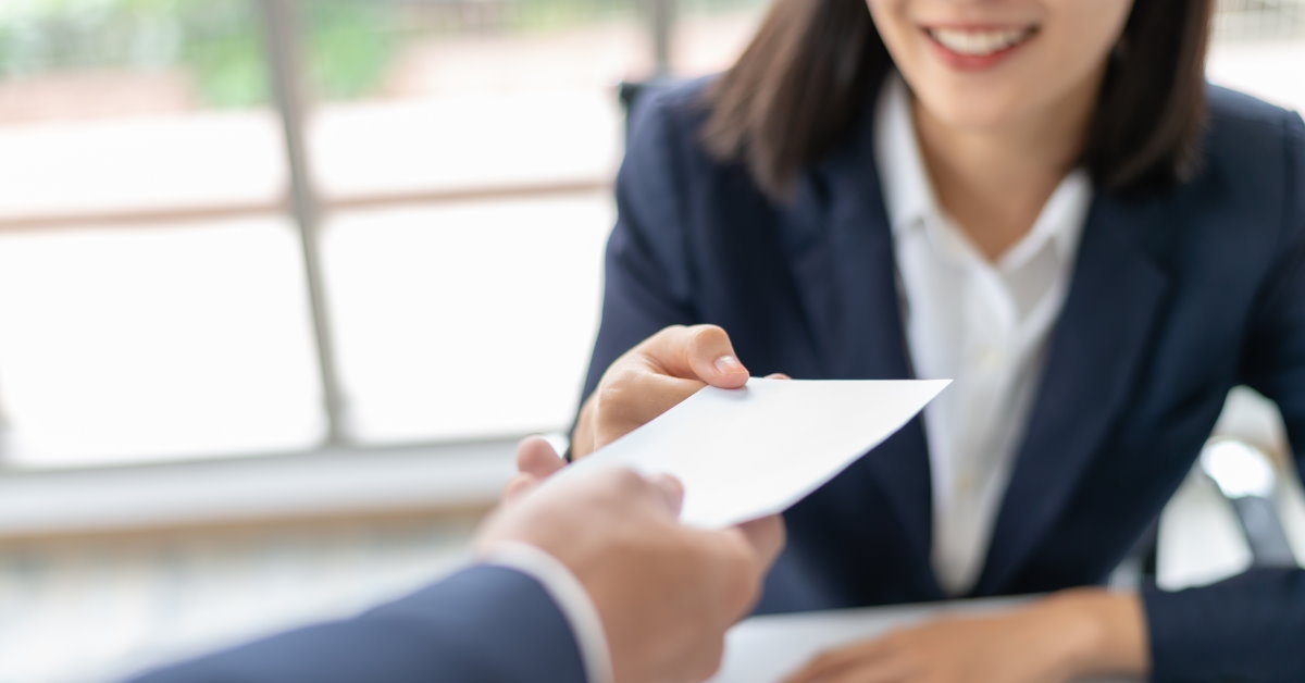 boss lady in suit giving salary to businessman in suit at office with laptop on table