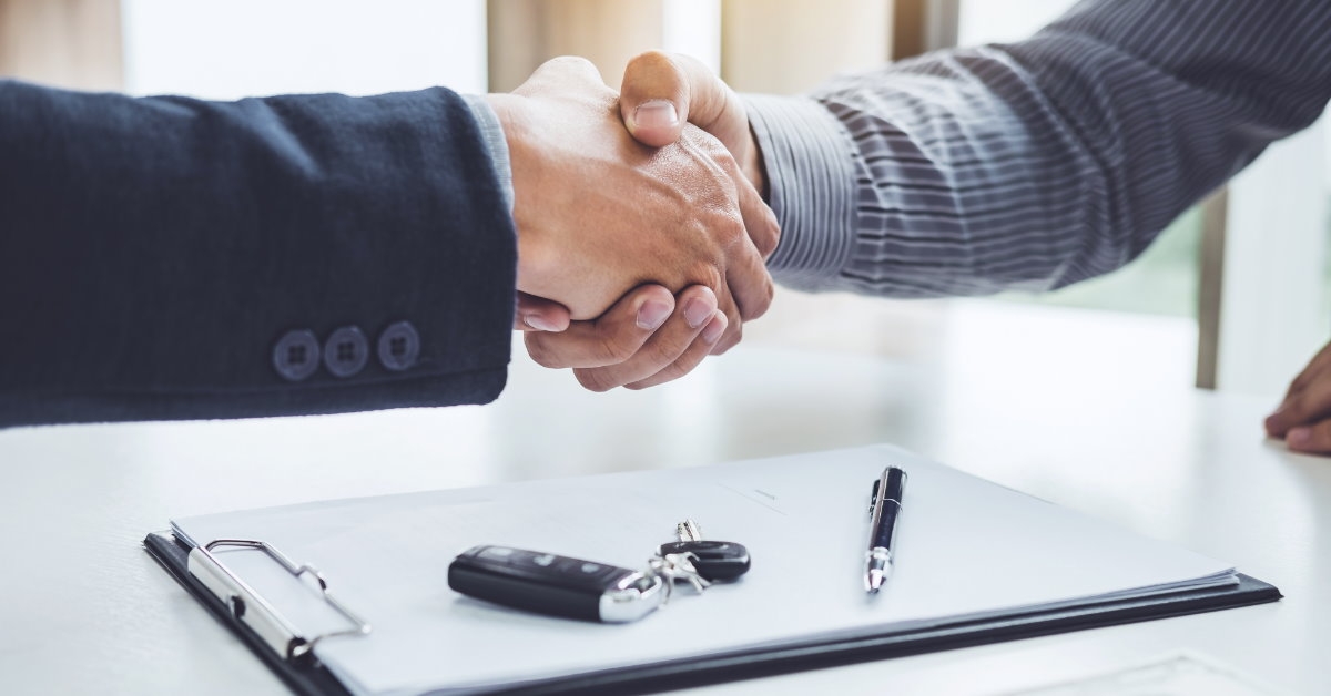 businessman shaking hand with salesman after purchasing new car with keys papers and pennies on table