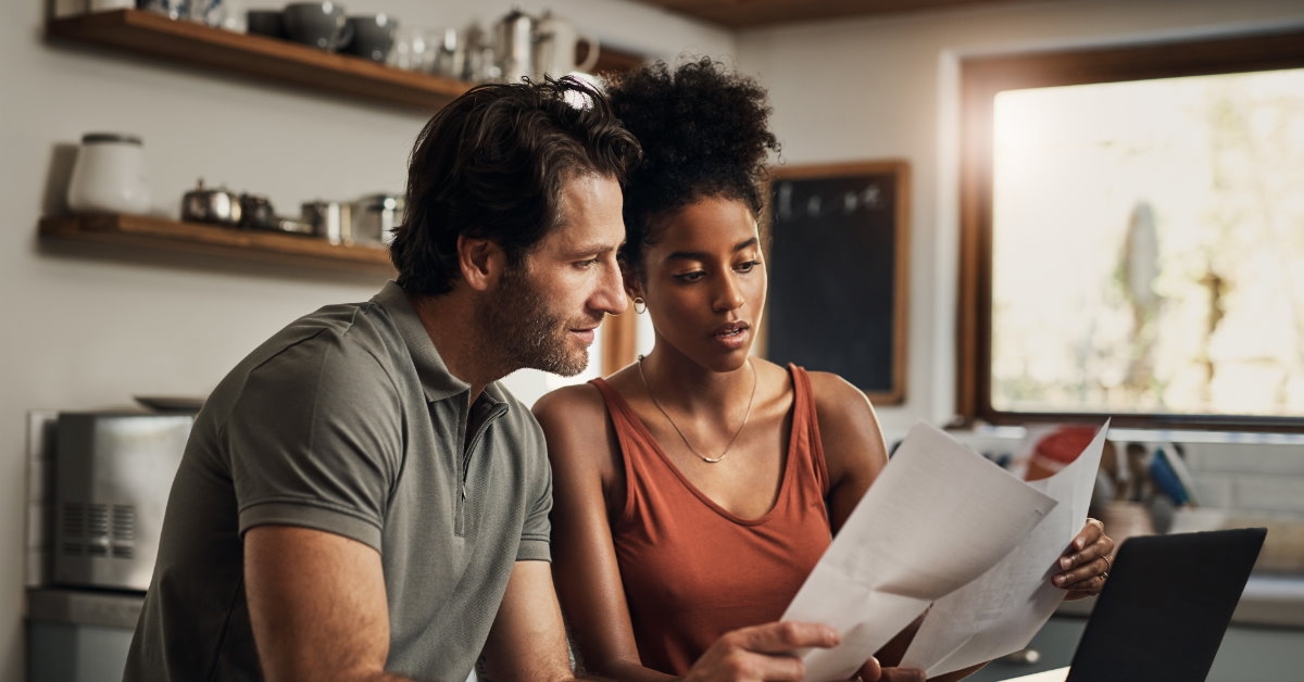 couple sitting on countertop at kitchen reviewing monthly budget on papers