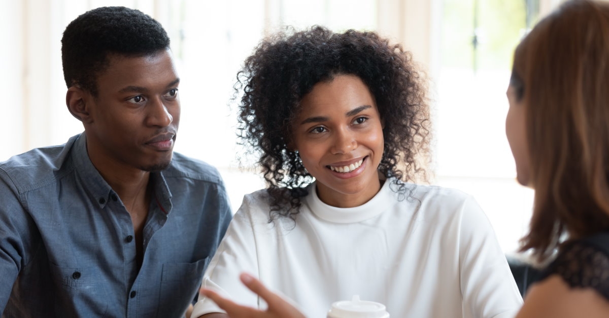 female real estate agent sitting across african american couple on table with coffee discussing mortgage