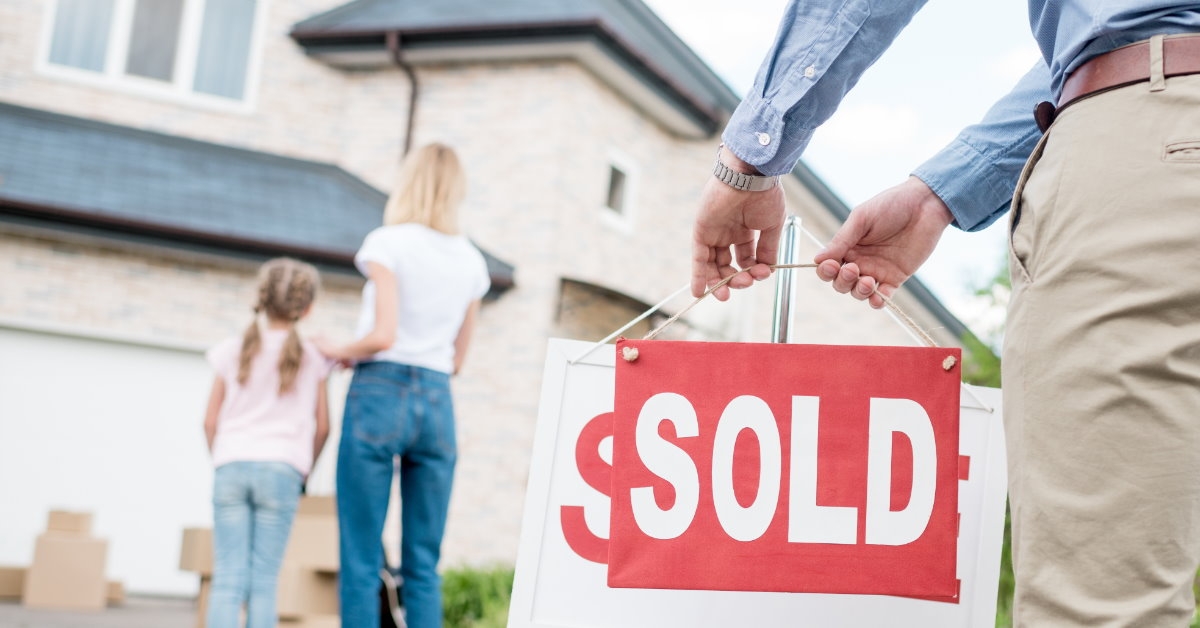 male realtor standing outside house hanging sold sign