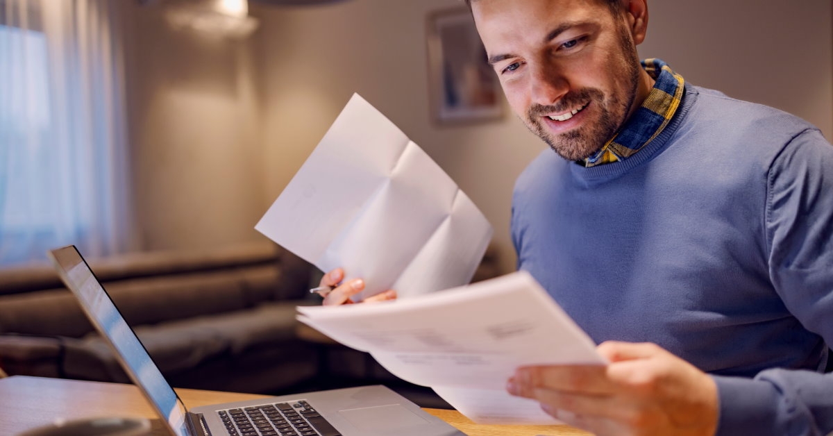 man sitting at table in front of laptop reviewing bills in hand