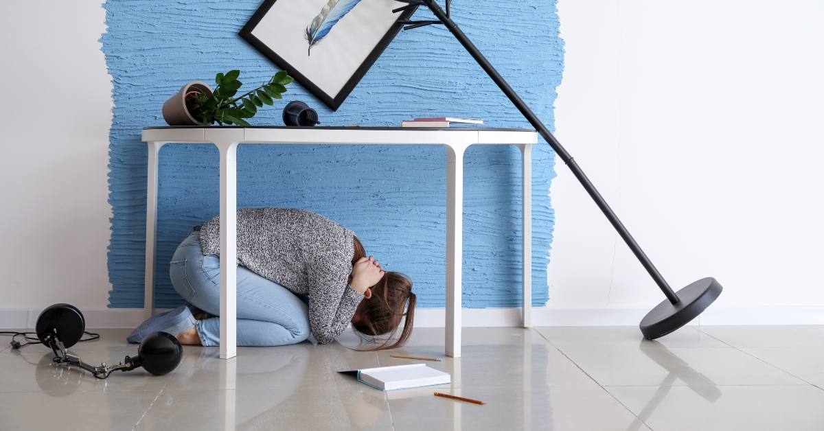 young woman hiding under table during earthquake