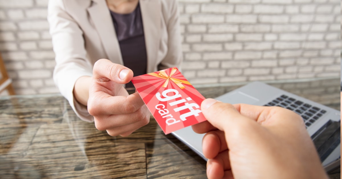 man giving gift card to businesswoman sitting in front of laptop at work