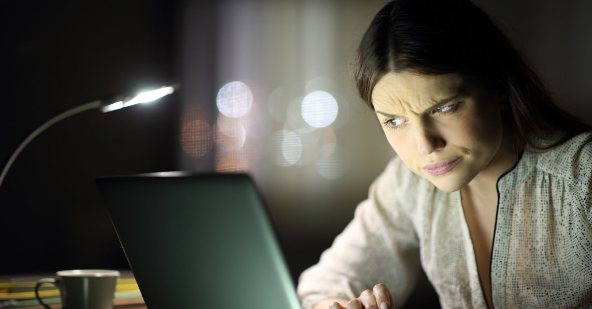 woman using laptop at night looking suspiciously at screen