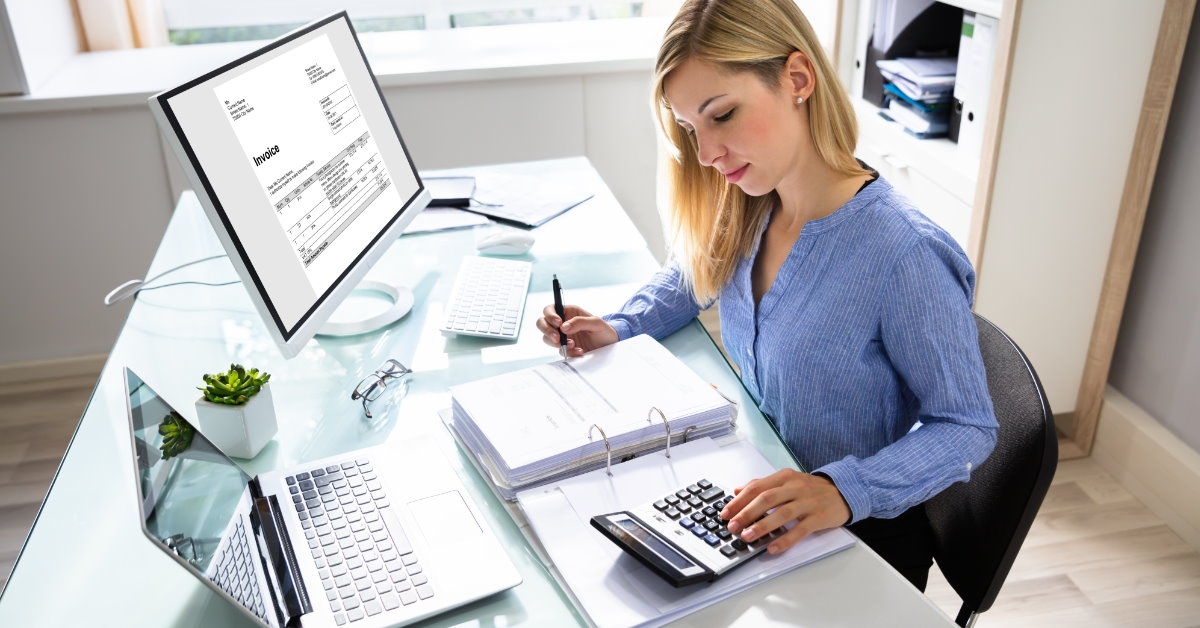 businesswoman sitting at table with documents desktop and laptop using calculator to calculate bills and finance