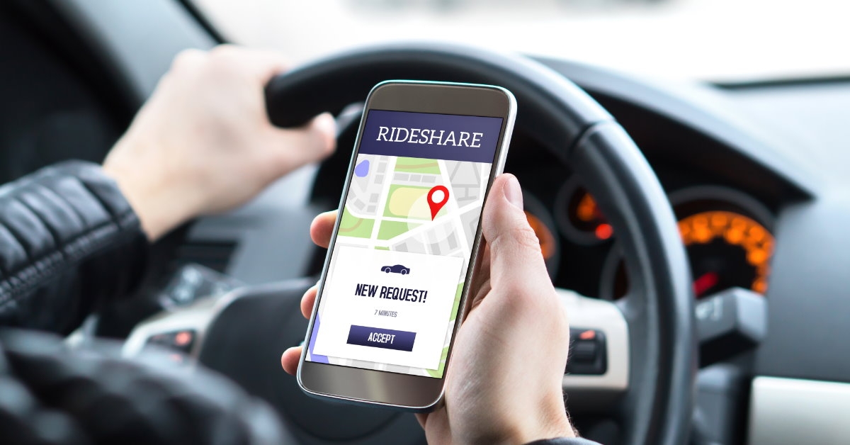 man sitting at driving seat holding smartphone with rideshare request on road