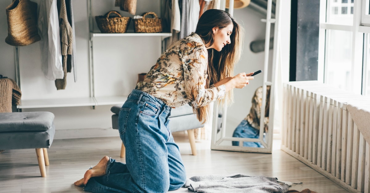 woman on knees in wardrobe capturing pictures of shirts in smartphone to sell