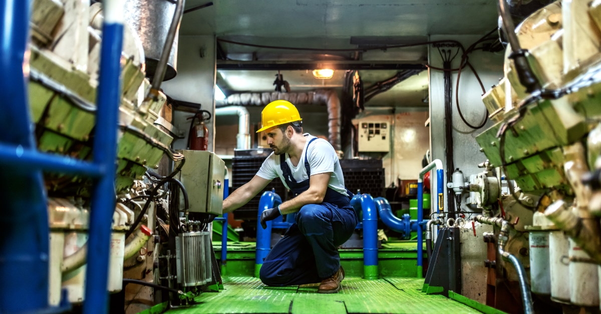 mechanic on his knees repairing the inside of a ship engine
