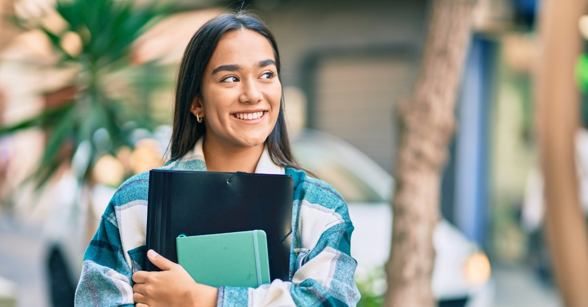 happy female student standing in street holding documents