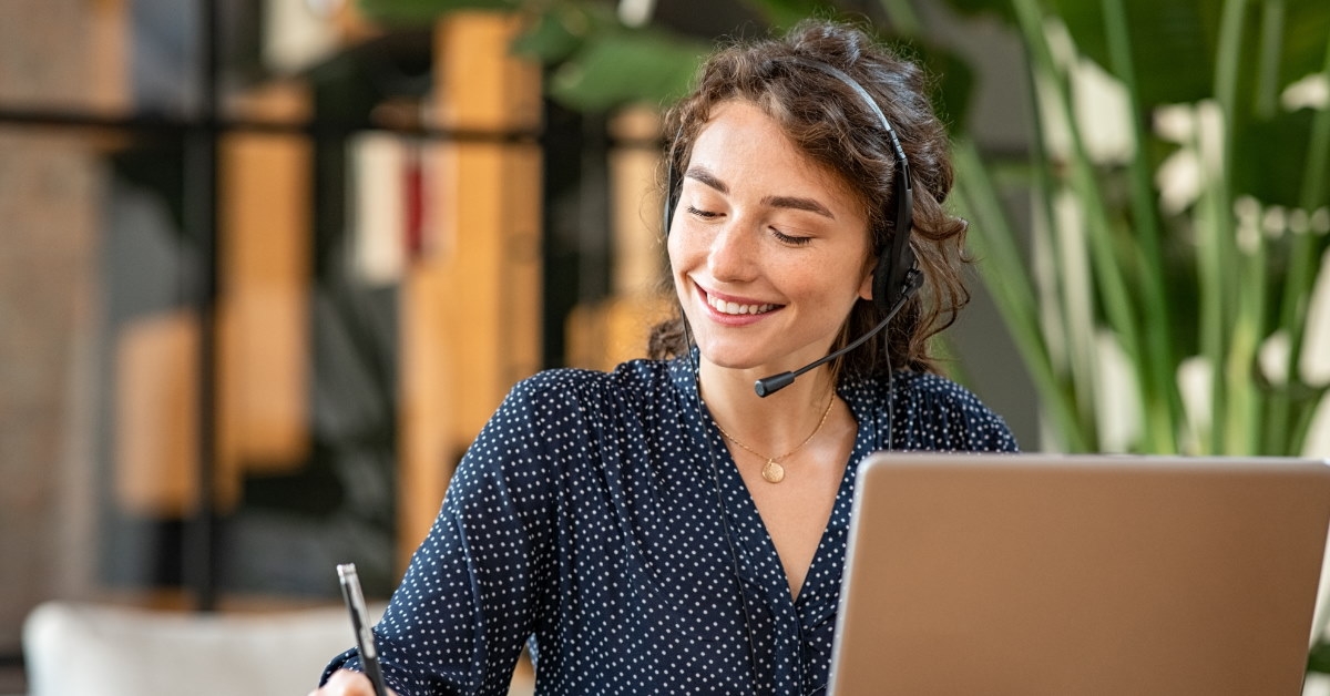 female customer service representative at office using laptop writing on notepad