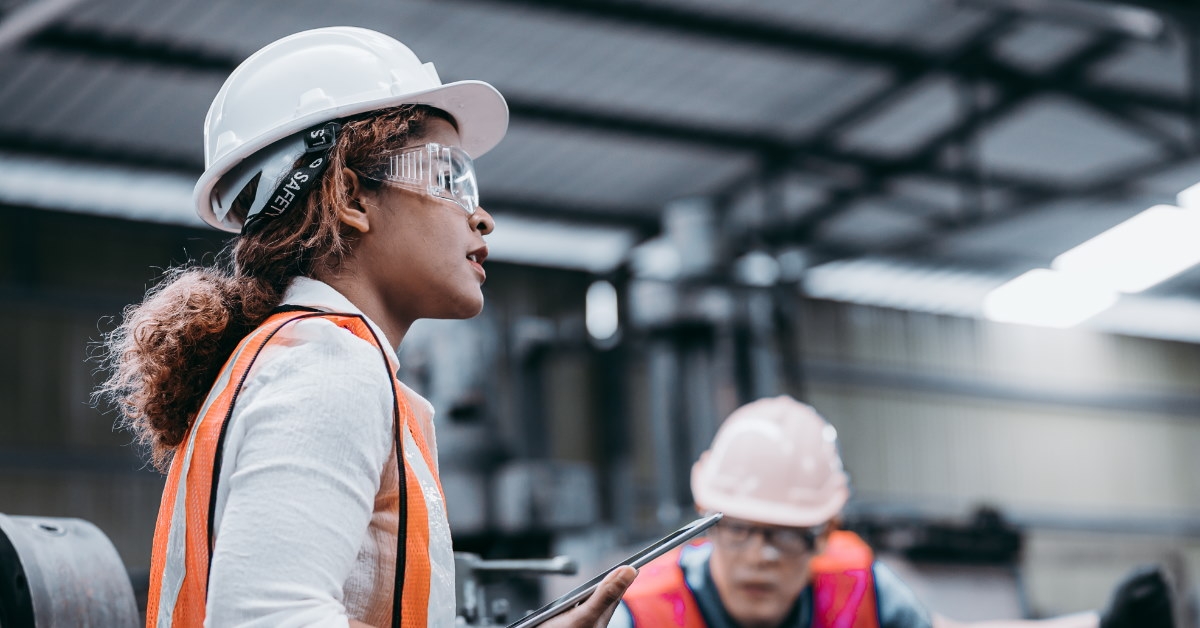 female industrial engineer wearing hat and uniform talking to male workers at back