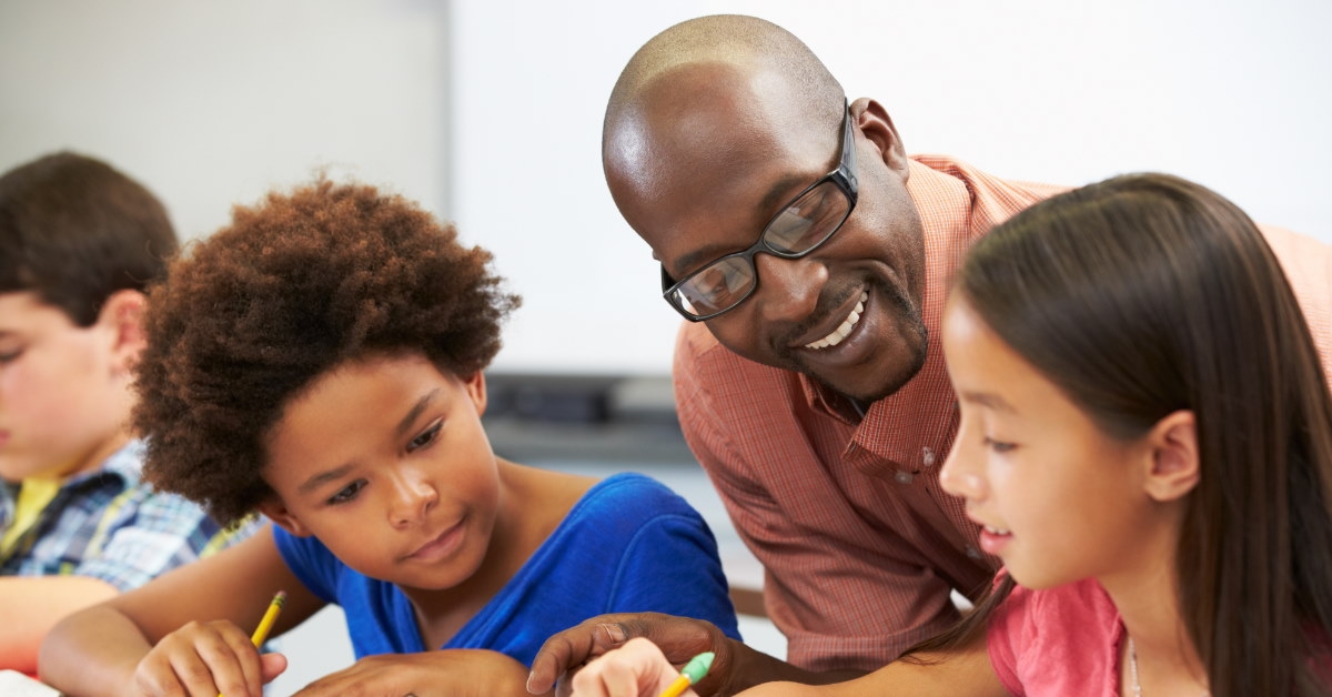 african american male teacher teaching students at desk in classroom
