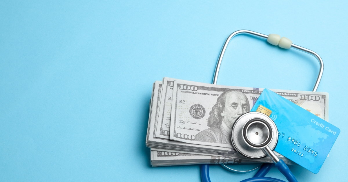 stethoscope and credit card on stack of cash on bluebackground