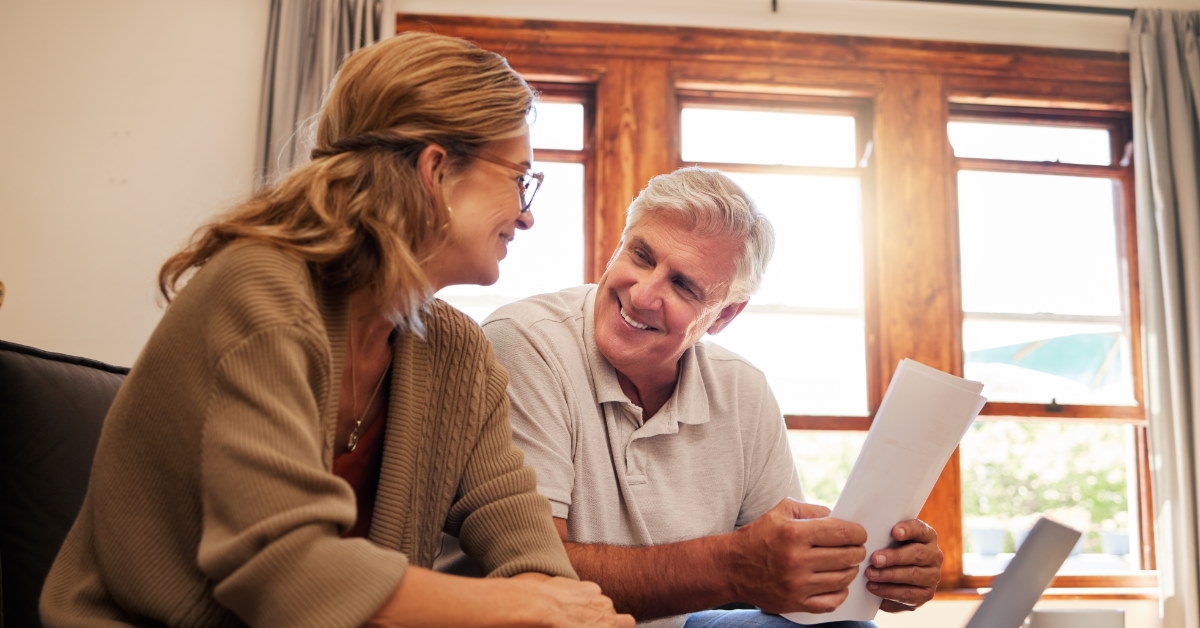 happy senior couple sitting on couch reviewing retirement documents