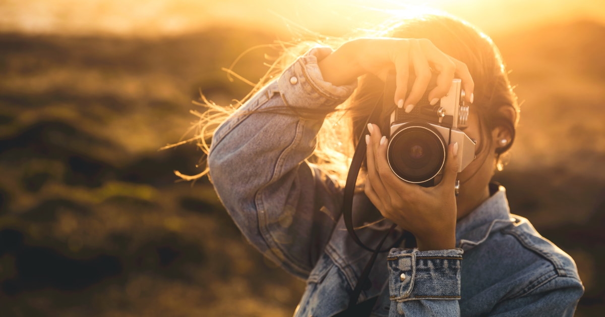 young woman wearing denim jacket posing with vintage camera outdoor
