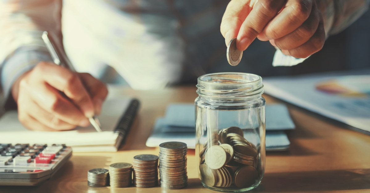 businessman saving pennies in jar while writing on notebook