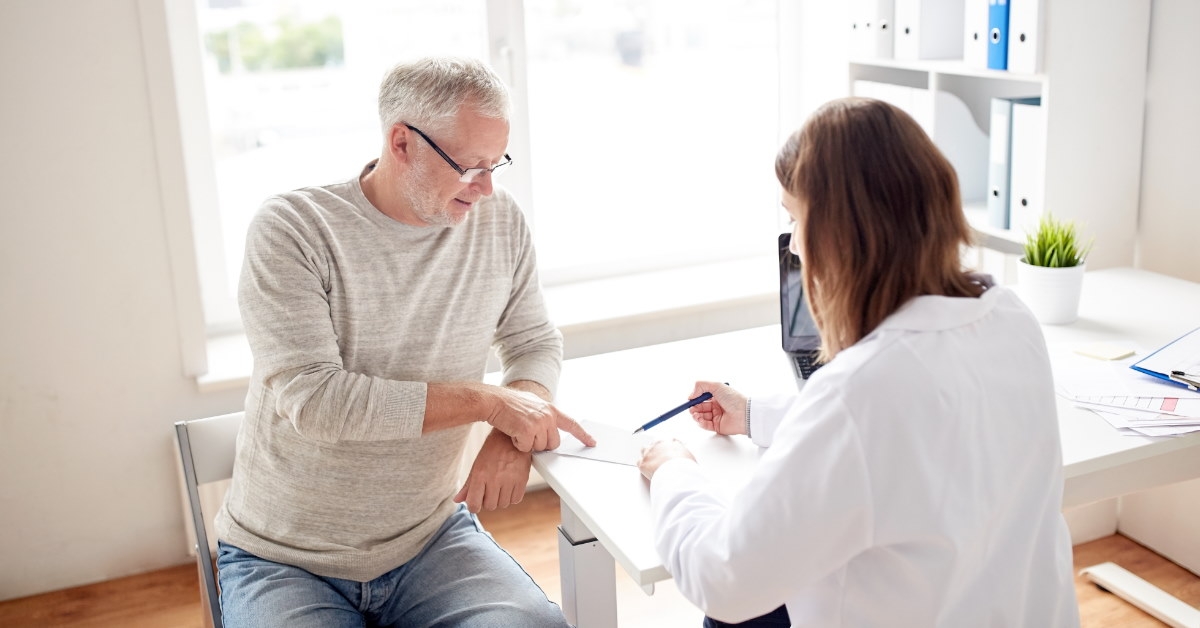 female doctor sitting in her clinic reading prcription to senior male pateint