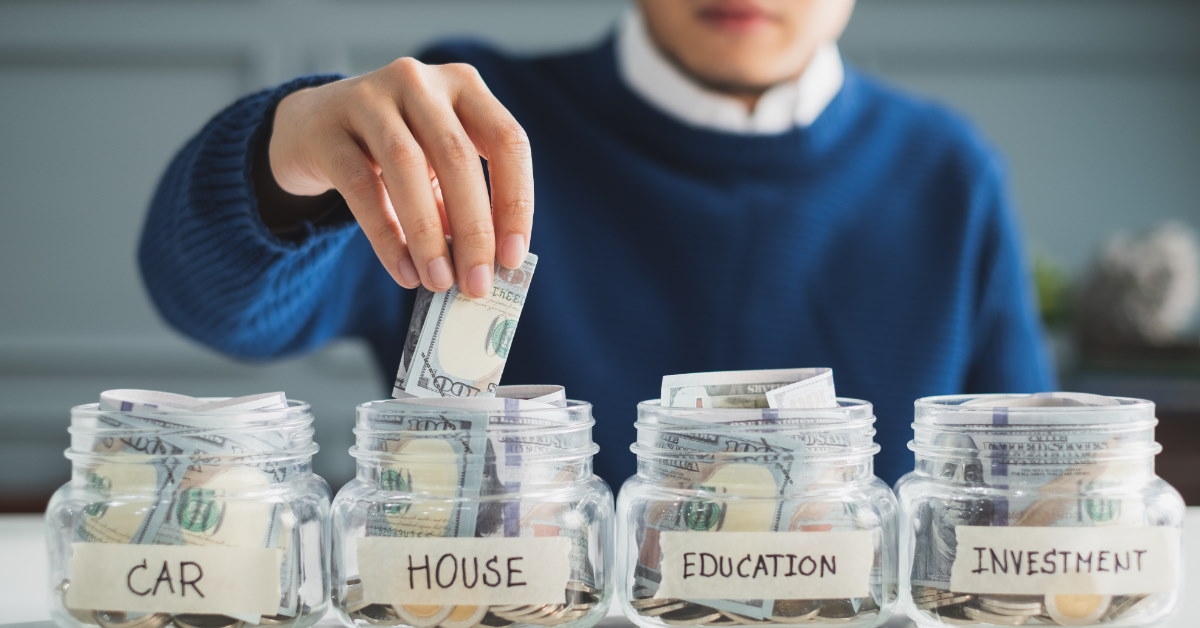 man saving money in labeled glass jars for car, house, education, and investment