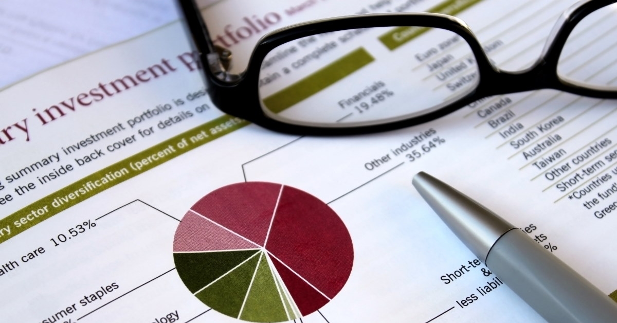 glasses and pen on top of financial portfolio with colorful graphs 