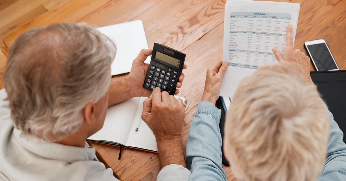 senior couple sitting on floor reviewing bills while using calculator at home