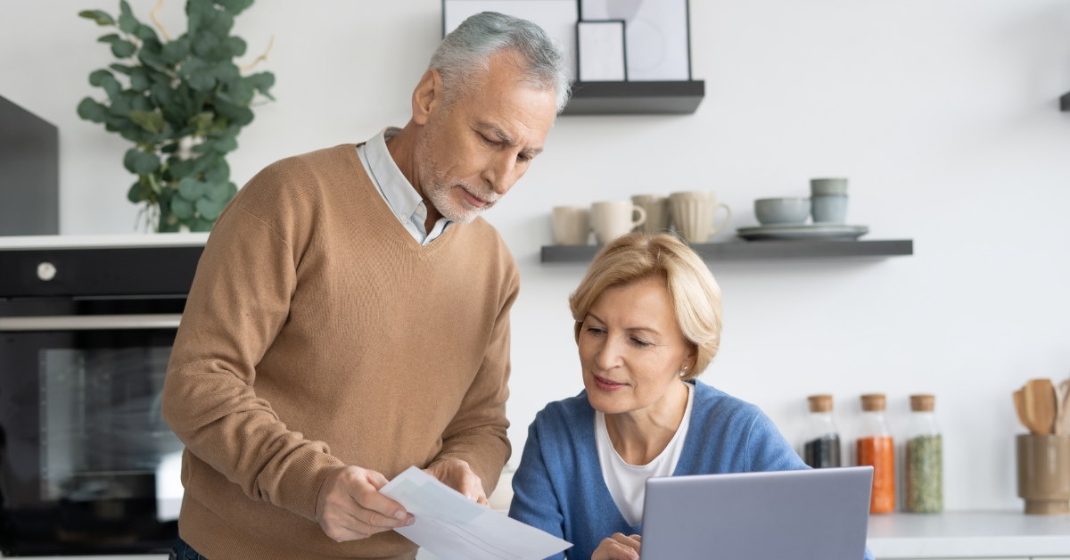 senior man showing papers to wife using laptop