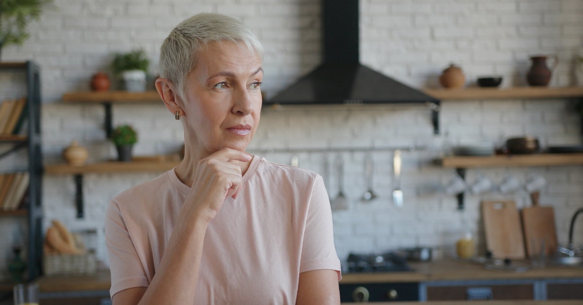 senior woman wearing pink shirt thinking in kitchen