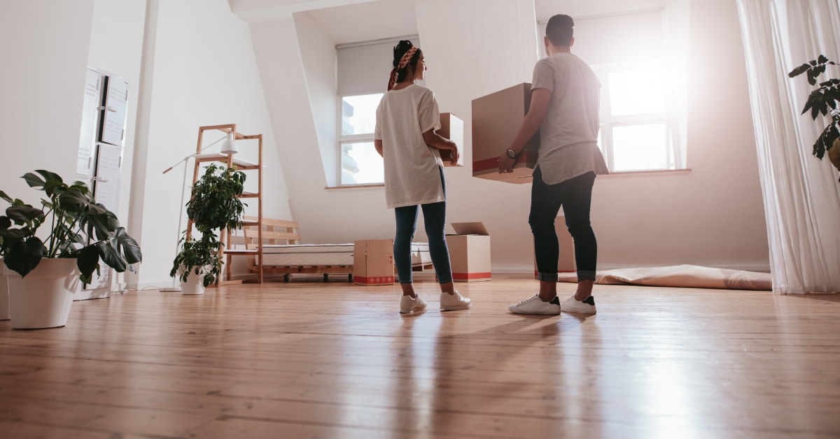 young couple standing in spacious lounge of new house holding moving boxes
