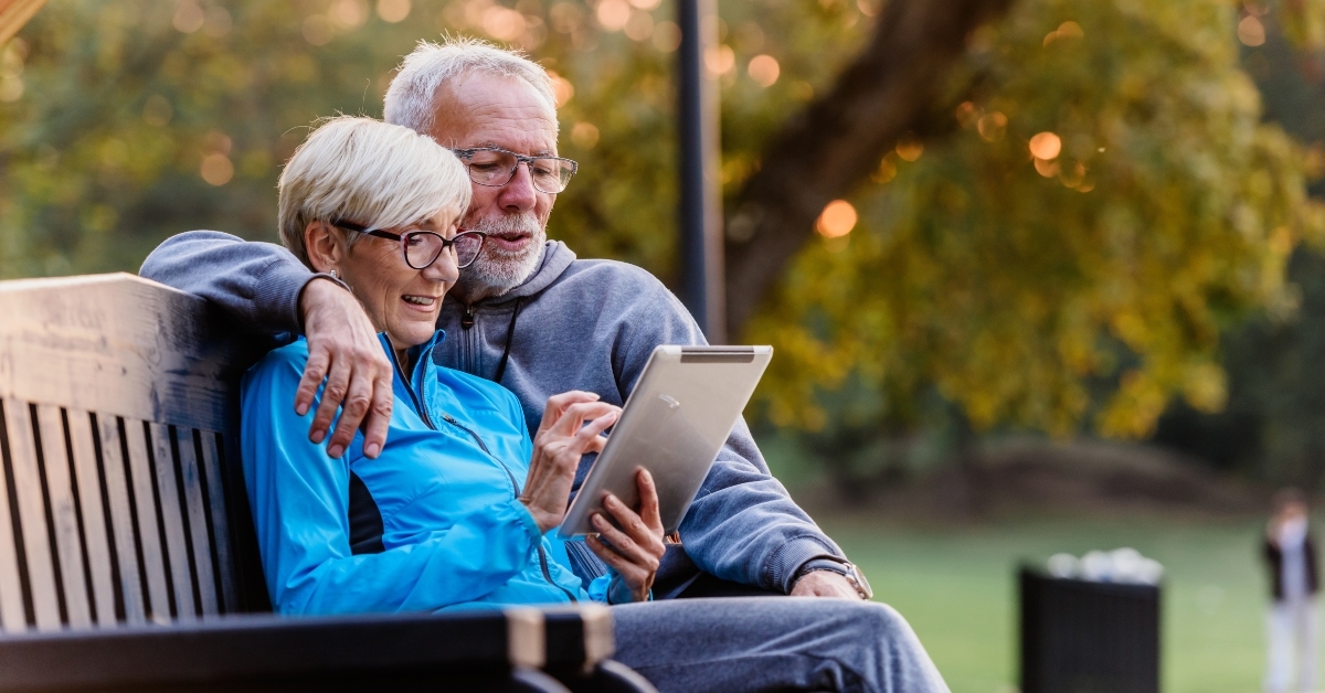 senior couple sitting on the bench looking at tablet computer