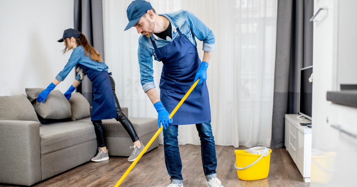 male and female professional cleaners mopping floor and dusting couch 