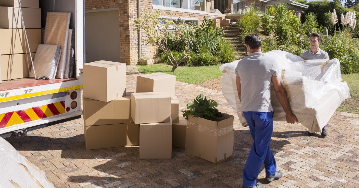 professional mowers standing outside new home with moving boxes in van taking sofa inside the house